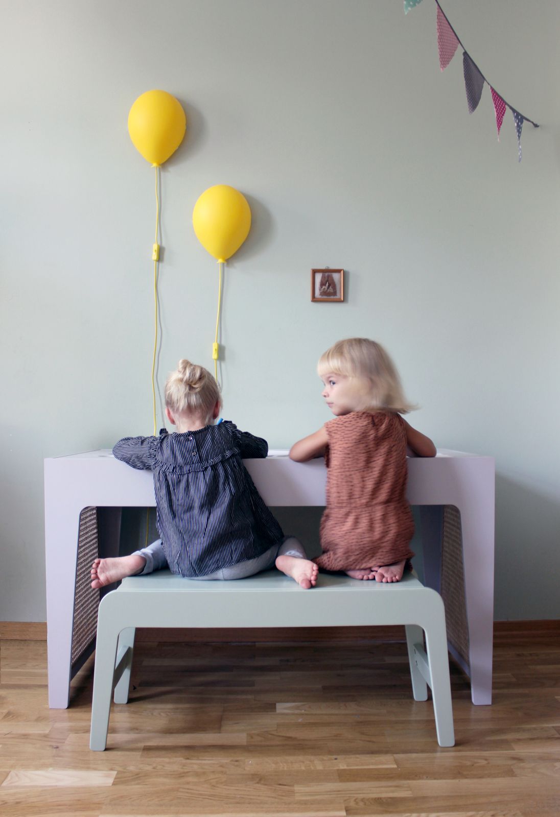 Kindertisch mit zwei kleinen Stühlen, darüber schweben bunte Ballonlampen an der Decke