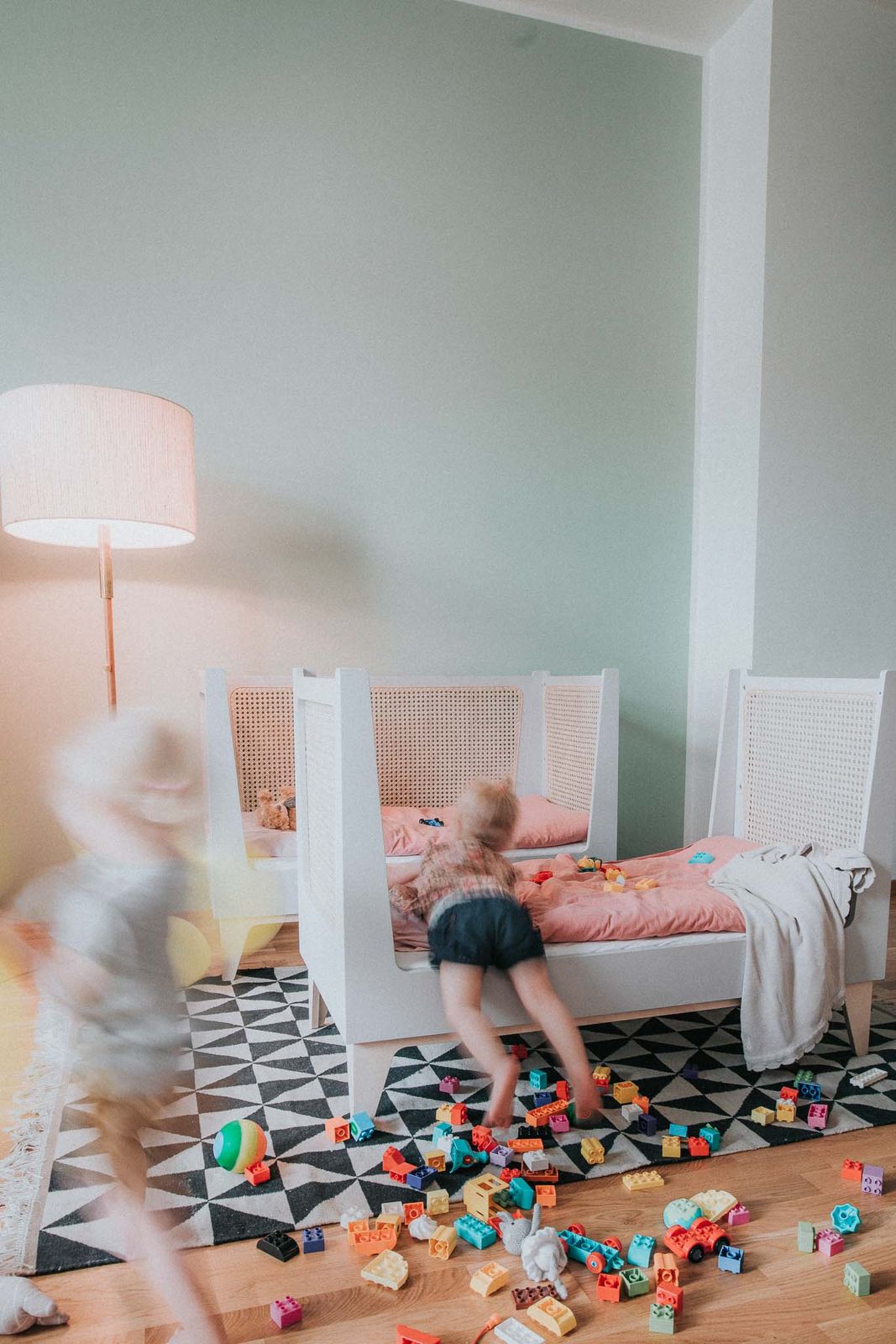 Zwei Kinder sitzen lachend im zusammengesetzten Zwillingsbett mit Wiener Geflecht